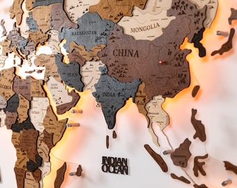 May include: A multi-layered wooden world map wall art piece featuring laser-cut continents in varying shades of brown and gray. The map includes engraved country names like China, India, and Kazakhstan, with warm LED backlighting.
