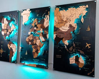 May include: A three-panel wooden world map wall art set featuring laser-cut continents in varying shades of brown wood. The map is mounted on dark panels with vibrant teal LED backlighting, displaying geographic labels and icons.