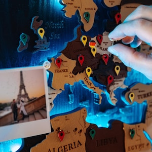 A hand is placing a small object on a map of Europe, which is decorated with various country shapes and labels.