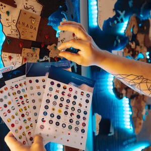 A person's hand is holding a stack of cards with various country flags, against a backdrop of a world map with blue lighting.