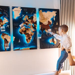 A woman holds a young child in front of a large world map with three panels, each depicting different regions of the world.