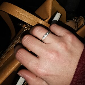 K&ouml;nnte beinhalten: Eine Hand mit einem silbernen Ring mit strukturiertem Design. Die Hand greift in eine braune Ledertasche.