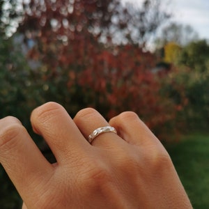 K&ouml;nnte beinhalten: Ein silberner Ring mit geometrischem Design. Der Ring wird an einem Finger getragen.