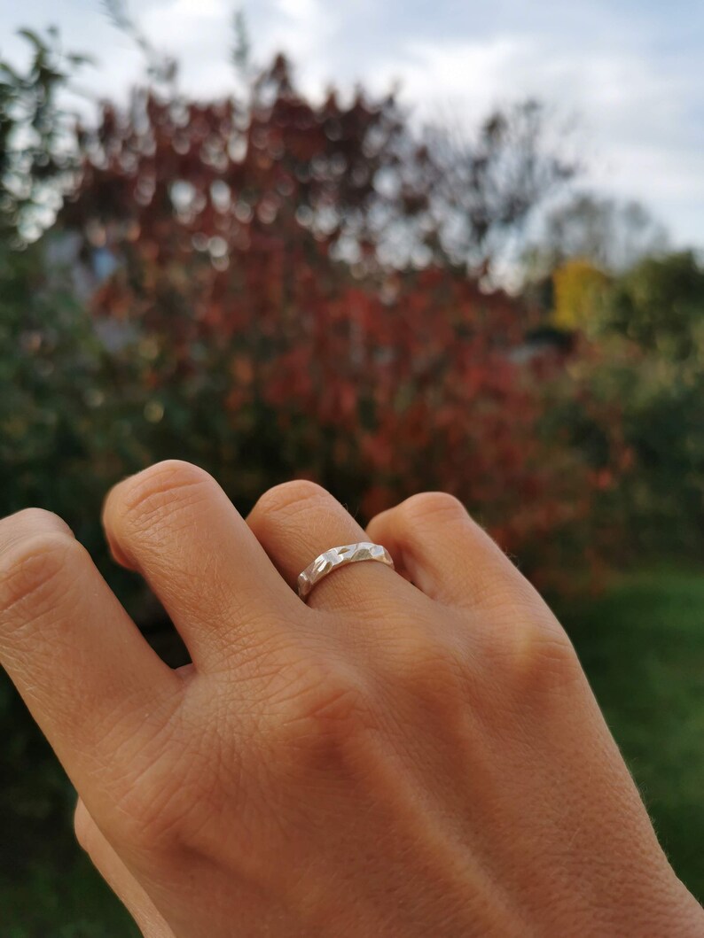 K&ouml;nnte beinhalten: Ein silberner Ring mit geometrischem Design. Der Ring wird an einem Finger getragen.