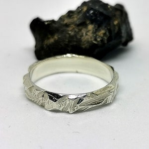 K&ouml;nnte beinhalten: Ein silberner Ring mit einer strukturierten, geh&auml;mmerten Oberfl&auml;che. Der Ring ist schlicht und elegant.