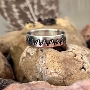 May include: A silver ring with a flame design. The ring is set on a light brown stone. The flame design is cut out around the band of the ring. The ring is a simple band style.