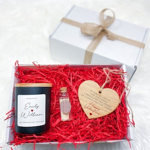 May include: A gift box filled with red shredded paper, a black candle with a wooden lid, a small glass bottle with matches, and a wooden heart-shaped ornament with the text "If I had my life to live over again I would find you sooner so I could love you longer Happy Valentines".