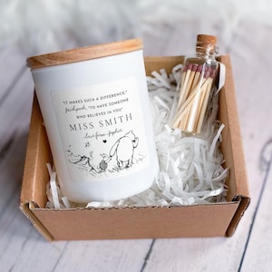 May include: A white candle in a glass jar with a wooden lid, featuring a label with Winnie the Pooh and Piglet illustrations and the text: "IT MAKES SUCH A DIFFERENCE, SAID POOH, TO HAVE SOMEONE WHO BELIEVES IN YOU" MISS SMITH love from Sophie.