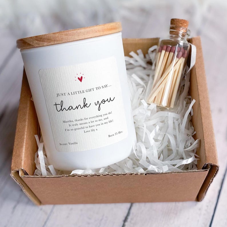 Peut inclure: Une bougie blanche avec un couvercle en bois et une &eacute;tiquette &laquo;&nbsp;merci&nbsp;&raquo; dans une bo&icirc;te cadeau avec une petite bouteille d'allumettes. La bougie a un parfum de vanille et br&ucirc;le pendant 25 heures.