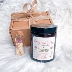 May include: A brown gift box with a brown ribbon and a brown candle with a label that says "Happy Mother's Day to a wonderful Mum" and a small glass jar with matches.