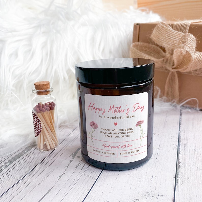 May include: A brown glass candle with a black lid and a white label that says "Happy Mother's Day to a wonderful Mum". The label also includes a pink carnation graphic, a heart, and the text "Thank you for being such an amazing Mum. I love you. Olivia. Hand-poured with love. Scent: Lavender. Burn 25 hours."