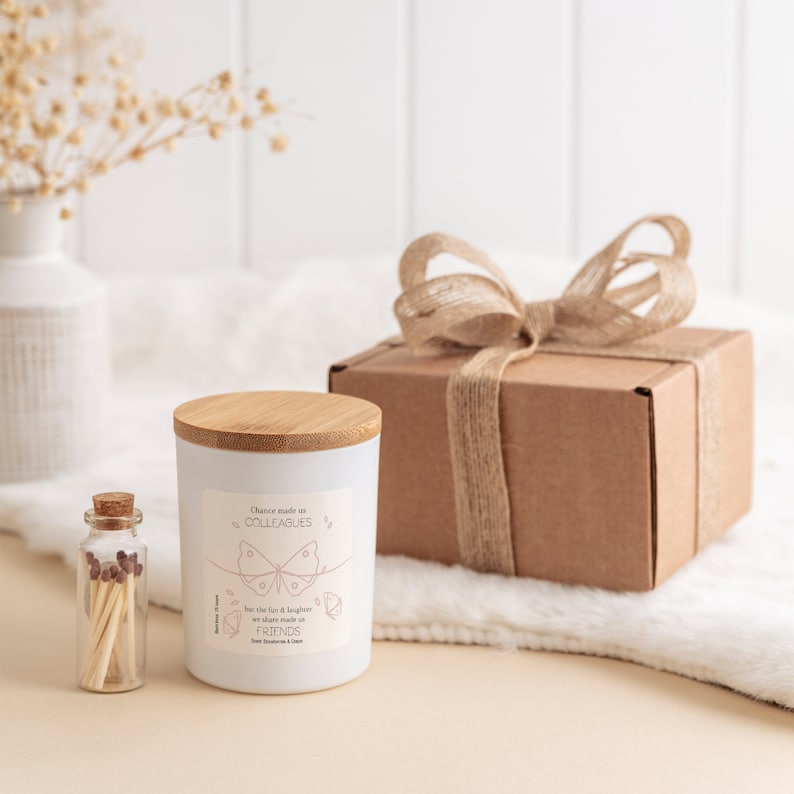 May include: A white candle with a bamboo lid and a pink butterfly design. The candle has the text "Chance made us colleagues but the fun & laughter we share made us friends."  The candle is packaged in a brown box with a hessian ribbon.