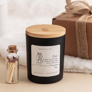 May include: Black candle with a wooden lid and a white label that says "Dad I'll always be your little girl Thanks for always being there no matter what I love you Kate" and "HAND-POURED with LOVE", "SCENT: LAVENDER", and "BURN TIME: 25 HOURS".