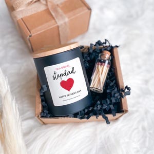 May include: A black candle with a wooden lid and a label that reads "TO A SPECIAL stepdad" with a red heart and "HAPPY FATHER'S DAY". The candle is in a gift box with matches.