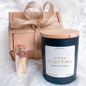 May include: A gift set featuring a black candle with a wooden lid, a small glass bottle of matches, and a wrapped box. The candle label reads "TO A SPECIAL STEP DAD MERRY CHRISTMAS". The candle is scented with Christmas Spice and burns for 25 hours.