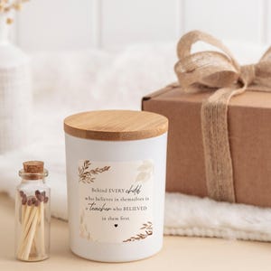 May include: A white candle in a cylindrical container with a bamboo lid, featuring a label with brown botanical illustrations and the text: Behind EVERY child who believes in themselves is a teacher who BELIEVED in them first. Includes a small glass bottle of matches.
