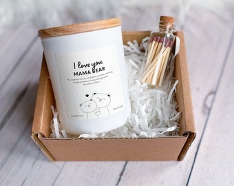 May include: A white candle with a wooden lid in a brown box with white shredded paper. The candle has a label that says "I love you Mama Bear" with a drawing of two bears hugging. A small glass jar with matches is also in the box.