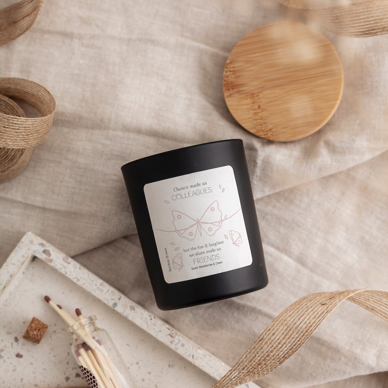 May include: Black candle jar with a white label that reads "Chance made us colleagues but the fun & laughter we share made us friends". The label features a butterfly graphic.