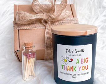 Puede incluir: Una vela negra con tapa de madera y una etiqueta que dice "Mrs. Smith, Just Wanted to Say A Big Thank You". También hay una pequeña botella de vidrio con cerillas y una caja de regalo atada con hilo.