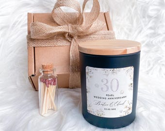 May include: A black candle with a wooden lid and a label that reads "30 Pearl Wedding Anniversary". A small glass bottle of matches and a gift box tied with twine are also present.
