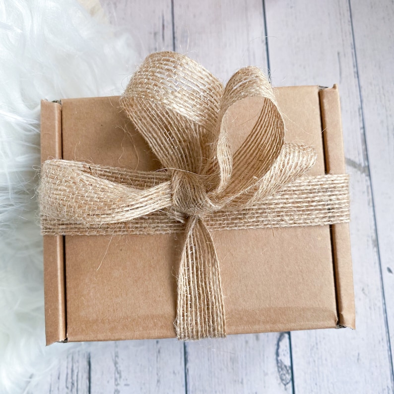 May include: A brown cardboard box with a burlap ribbon tied in a bow. The box is sitting on a white wooden surface.