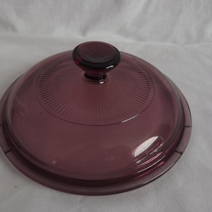 May include: A purple glass lid with a knob on top. The lid has a textured, ribbed design.