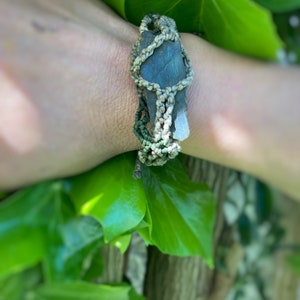 Puede incluir: Un brazalete de piedra verde y gris con un diseño de nudo macramé.