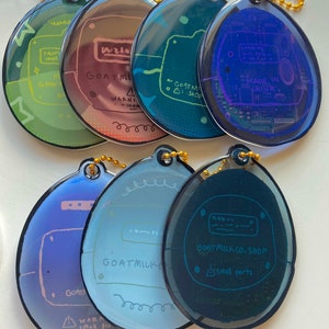 May include: A set of ten colorful, round keychains with a circuit board design. Each keychain features a different color gradient and includes the text "GOAT MILK CO. SHOP" and a warning about small parts.