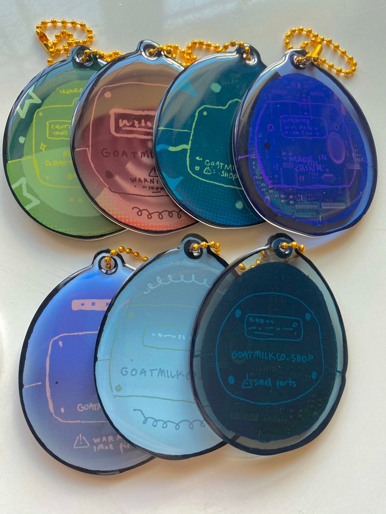 May include: A set of ten colorful, round keychains with a circuit board design. Each keychain features a different color gradient and includes the text "GOAT MILK CO. SHOP" and a warning about small parts.