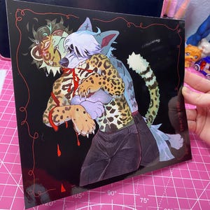 Pode incluir: Uma impressão artística quadrada sobre um fundo preto com uma ilustração estilizada de dois personagens antropomórficos. Um personagem tem pelo com estampa de leopardo e calças escuras, enquanto o outro tem pelo azul claro e cabelo branco. Líquido vermelho escorre.