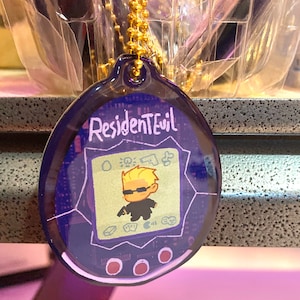 May include: A purple and blue plastic keychain shaped like a digital pet with a cartoon image of a character from the video game Resident Evil. The keychain has the text "Resident Evil" on the top.