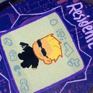 May include: A purple and white digital pet keychain with a cartoon character on the screen. The screen reads "Resident Evil".