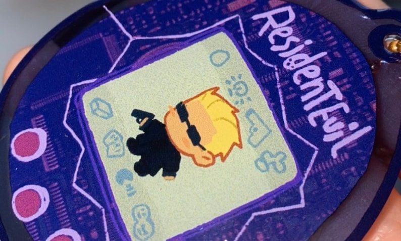 May include: A purple and white digital pet keychain with a cartoon character on the screen. The screen reads "Resident Evil".