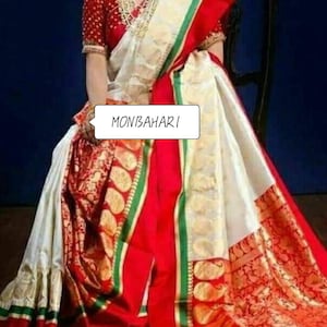 May include: A traditional Indian saree in white, red, and gold. The saree features intricate gold patterns and a red border with green accents. The text "MONBAHARI" is visible on the saree.