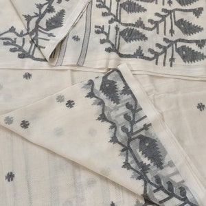 Könnte beinhalten: Ein cremeweißes Textil mit einem dunkelgrauen Webmuster aus stilisierten Blättern und Zweigen. Der Stoff zeigt ein sich wiederholendes botanisches Motiv entlang der Ränder und verstreute kleine geometrische Formen auf dem Hauptteil.