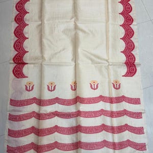 May include: A cream-coloured textile featuring a red scalloped border pattern along the sides and bottom. The fabric displays a series of small, stylised floral motifs in red and yellow arranged in a horizontal row above the lower border.