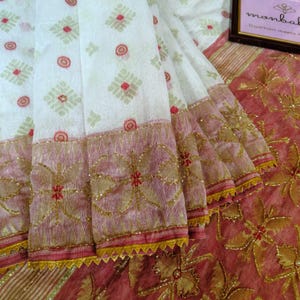 May include: A white fabric featuring a repeating pattern of small red circles and light green geometric shapes. The fabric has a wide border in a dusty rose colour with gold embroidery and a yellow serrated edge. A small sign reads monbal.