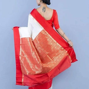May include: A white and red saree with a gold patterned border. The saree is draped over the shoulders and arms. The model is wearing a red blouse with short sleeves.