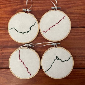 May include: Four embroidery hoops with white fabric and different colored embroidery designs. The designs are a green wavy line, a red wavy line, a red wavy line, and a green wavy line.