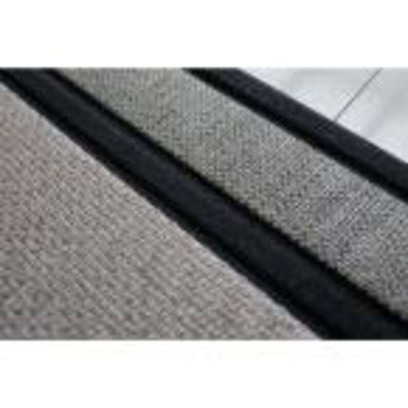 May include: Close-up of a gray and black woven rug with a black border. The rug has a textured surface.