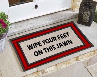 May include: A beige doormat with a red border and the text "Wipe your feet on this Jawn" in black.