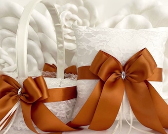 May include: White lace ring pillow with a large burnt orange satin bow and a small rhinestone in the center. A matching burnt orange satin bow decorates a white lace flower girl basket.