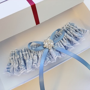 May include: A light blue garter with white lace and a blue satin bow. The garter has a small, round, silver-toned embellishment with clear rhinestones.