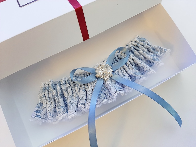 May include: A light blue garter with white lace and a blue satin bow. The garter has a small, round, silver-toned embellishment with clear rhinestones.