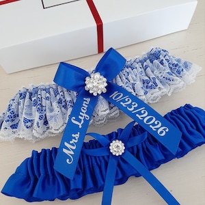 Peut inclure: Deux jarreti&egrave;res en satin bleu avec une bordure en dentelle blanche. Une jarreti&egrave;re est orn&eacute;e d'un strass argent&eacute; et l'autre d'une perle argent&eacute;e. Les jarreti&egrave;res sont personnalis&eacute;es avec le texte "Mrs. Lyons" et "10/23/2026".