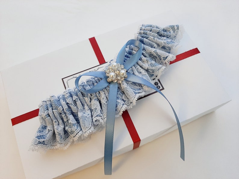 May include: A blue and white lace garter with a blue satin bow and a rhinestone and pearl embellishment.