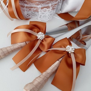 May include: Two cake cutting knives with brown satin ribbon bows and pearl embellishments. The knives have ivory handles.