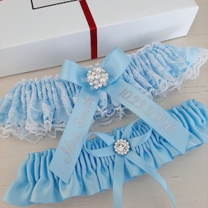 Peut inclure: Deux jarreti&egrave;res de mari&eacute;e bleu clair avec une bordure en dentelle blanche. La jarreti&egrave;re sup&eacute;rieure est orn&eacute;e d'un strass argent&eacute; et du texte "10.23.2026". La jarreti&egrave;re inf&eacute;rieure est orn&eacute;e d'un strass argent&eacute; et du texte "Mme Smith".