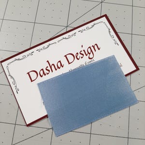 May include: A white business card with a red border and a decorative border design. The text "Dasha Design" is in red font. The text "Memorable Events" is in black font. A light blue ribbon is on top of the card.
