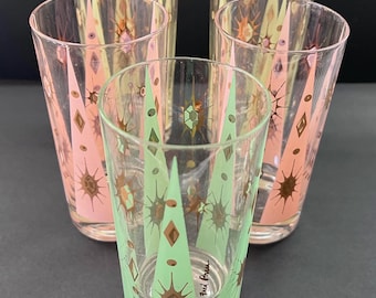 May include: Set of five vintage drinking glasses. Each glass features a clear body with a decorative pattern of pink, green, and gold geometric shapes. The glasses have a mid-century modern aesthetic.